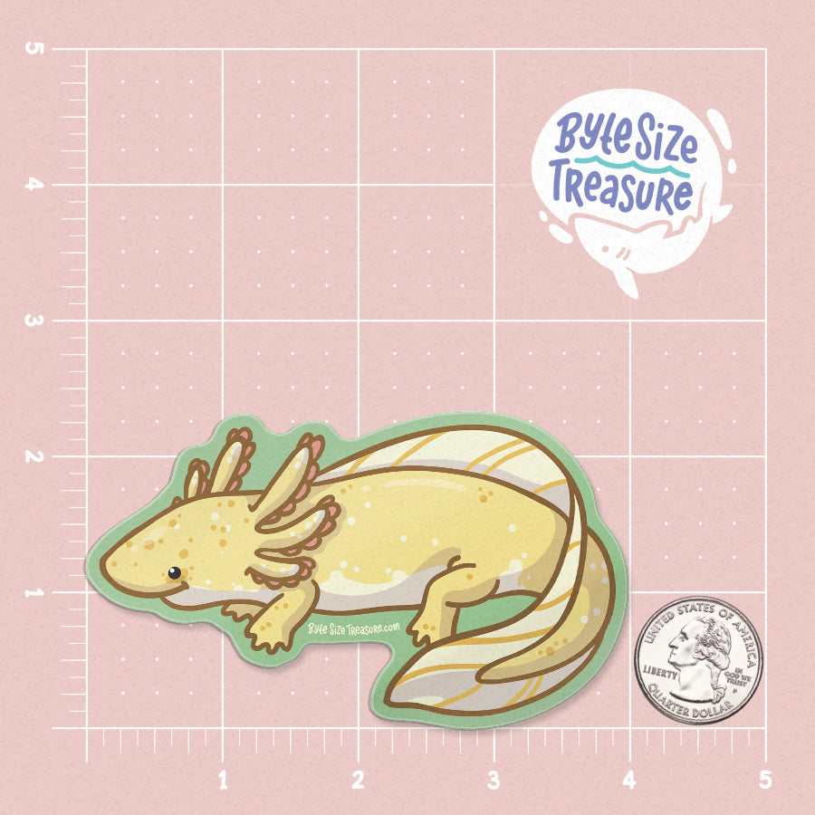 A golden yellow axolotl sticker - shown on a pink measuring grid background with a quarter for scale. Art by Byte Size Treasure
