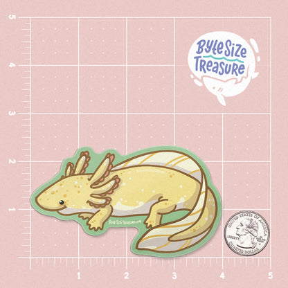 A golden yellow axolotl sticker - shown on a pink measuring grid background with a quarter for scale. Art by Byte Size Treasure