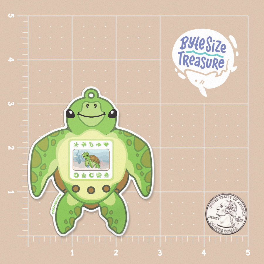 A silly sticker featuring tamagotchi in the shape of a sea turtle - shown on a tan measuring grid background with a quarter for scale. Art by Byte Size Treasure